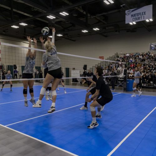 Woman spiking a volleyball toward defenders.